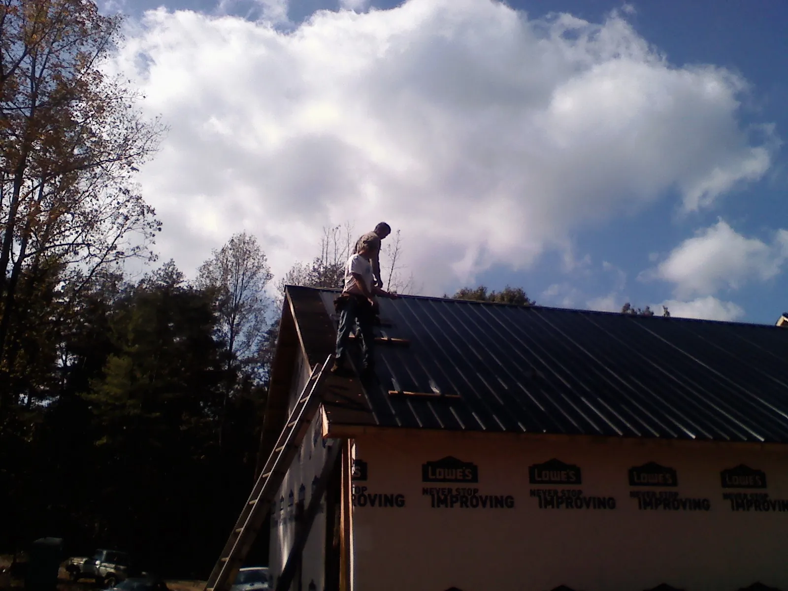 Roofer fastening dark metal panels high against a cloudy sky, from a Roof Inspection job in Middletown