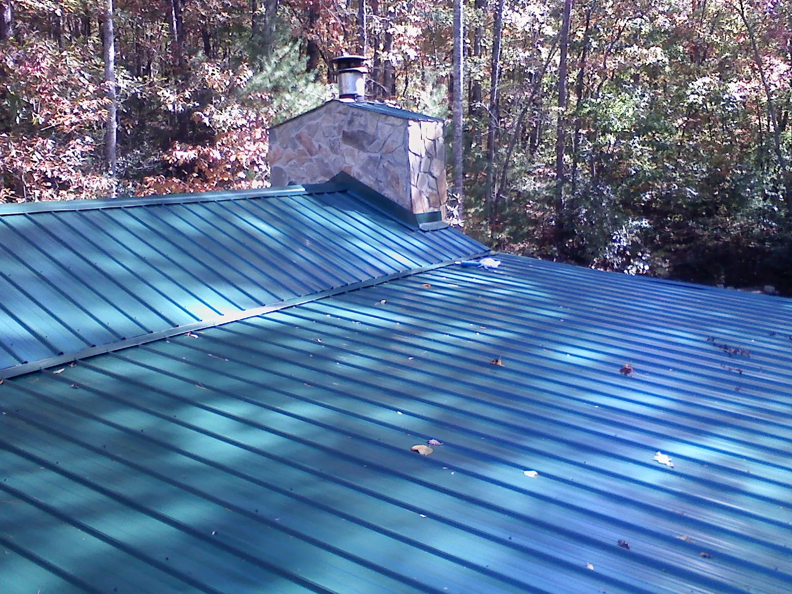 New green metal roof and stone chimney surrounded by autumn woods in Middletown
